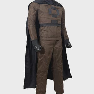 May include: A brown long-sleeved shirt and matching trousers costume set featuring a black cape, a high collar, and black rectangular patches on the chest. The sleeves have white stitched detailing, and the cuffs are ribbed in black fabric.
