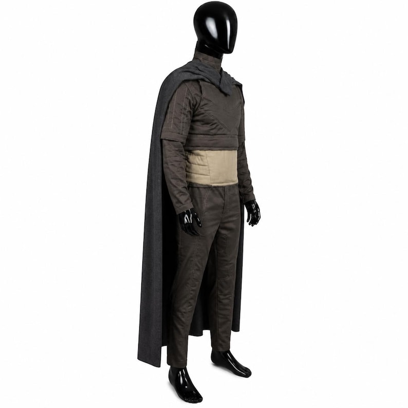 May include: A dark gray long-sleeved tunic and matching trousers set worn with a long, flowing dark gray cape. The outfit includes a wide, light tan horizontal waistband and features structured, quilted-style stitching on the upper sleeves.