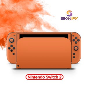 Könnte beinhalten: Eine einfarbig orangefarbene Spielkonsole mit passender Dockingstation, schwarzem Bildschirm und Controller-Tasten. Das Skinify-Logo befindet sich oben rechts, der Text Nintendo Switch 2 ist unten zentriert mit einem orangefarbenen Pulvereffekt.