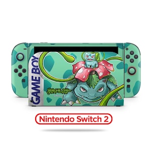 May include: A Nintendo Switch console featuring a custom design with a green and white color scheme. The design includes a large illustration of a Venusaur and Bulbasaur. The text "GAME BOY" and "Nintendo Switch 2" are also visible.