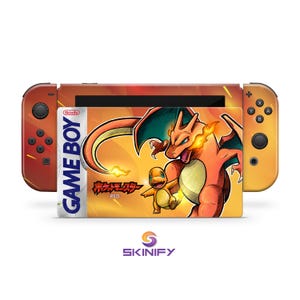 Peut inclure: Une console Nintendo Switch avec une peau personnalisée représentant Charizard et Charmander de la série Pokémon. La peau a un design de style Game Boy avec le texte "GAME BOY" et "RED". Les Joy-Cons de la console sont orange.