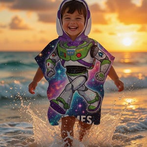 May include: A child wearing a hooded beach towel featuring a Buzz Lightyear design, running through the ocean water. The towel has a white hood and a colorful graphic of the character. The background shows a sunset over the ocean.