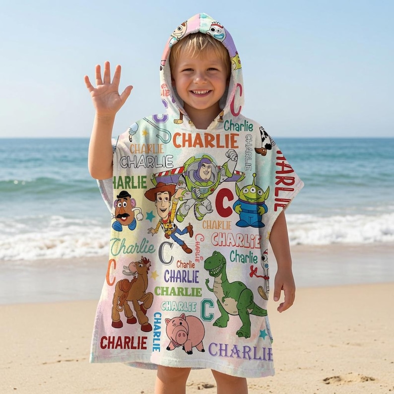 May include: A hooded poncho towel featuring a colorful Toy Story character print with Woody, Buzz Lightyear, Rex, and other figures. The design includes the name Charlie in various fonts and colors scattered across a light background.