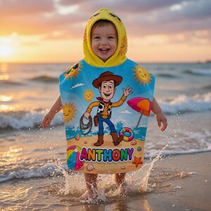 May include: A child wearing a blue and yellow hooded beach towel with a cartoon cowboy design, the name "ANTHONY" is printed on the towel. The child is standing in the ocean at sunset.