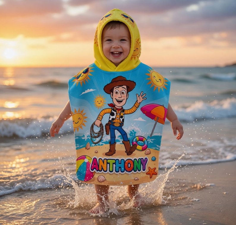May include: A child wearing a blue and yellow hooded beach towel with a cartoon cowboy design, the name "ANTHONY" is printed on the towel. The child is standing in the ocean at sunset.