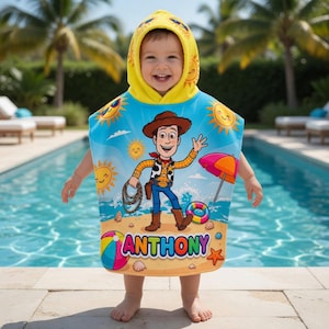 May include: A child wearing a hooded beach towel featuring a cartoon cowboy character, a beach scene, and the name "ANTHONY". The towel is blue with yellow trim and a hood with sun and smiley face designs.