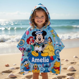 May include: A light blue hooded beach towel featuring Mickey Mouse in a sailor outfit, along with other Disney characters. The towel has the name "Amelia" on it. The background shows a beach and ocean.