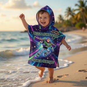 May include: A child's hooded poncho featuring Buzz Lightyear, in purple, blue, and green. The poncho has the words "Buzz Lightyear" and "Space Ranger". The background design is a starry night sky. The child is on a beach.