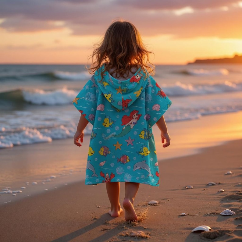 May include: A turquoise hooded beach towel featuring a mermaid and other sea creatures. The towel is worn by a child walking on a sandy beach at sunset. The towel's design includes fish, starfish, and seashells.