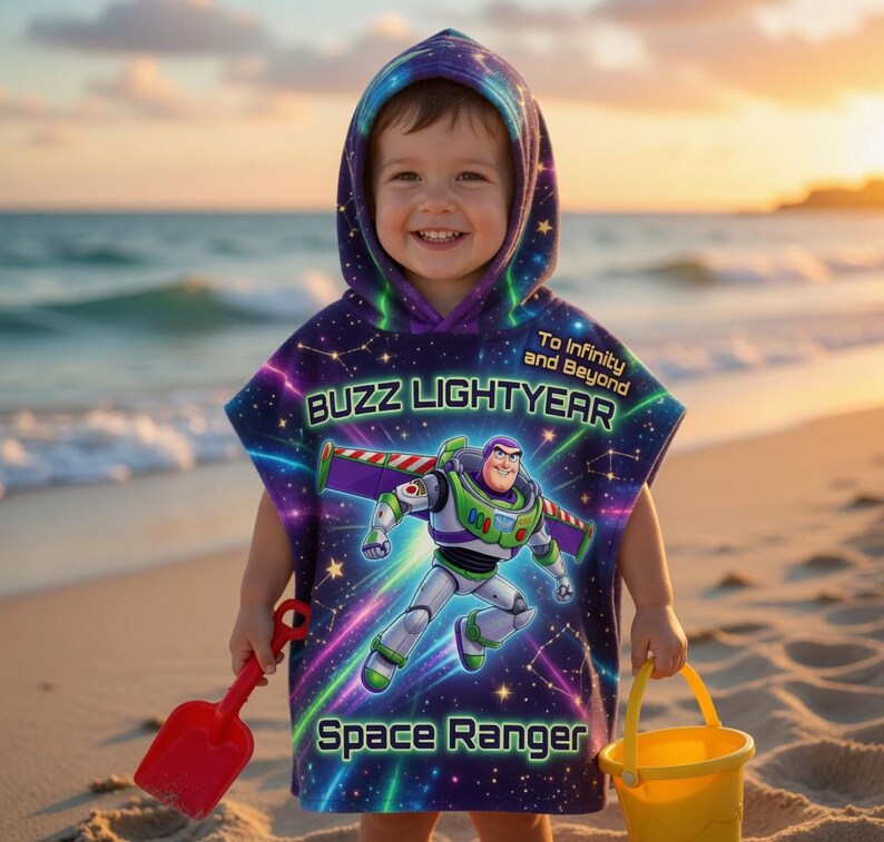 May include: A child wearing a purple and blue Buzz Lightyear hooded beach towel with the text "Buzz Lightyear" and "Space Ranger". The child is holding a red spade and a yellow bucket on a sandy beach.