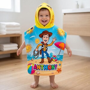 May include: A child wearing a hooded beach towel featuring a cartoon cowboy character. The towel is blue with a beach scene design, including suns, an umbrella, and the name "ANTHONY". The hood is yellow with sun graphics.