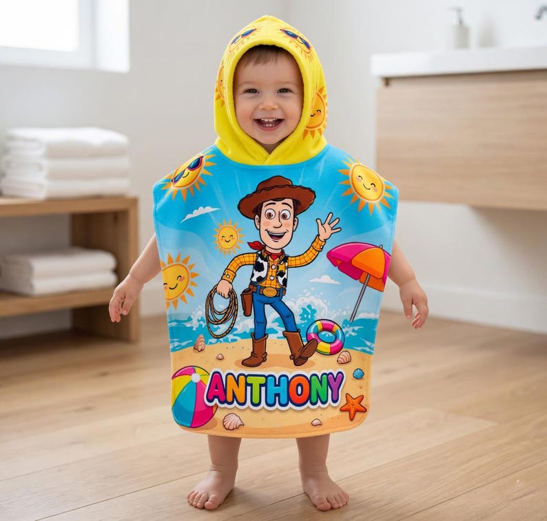 May include: A child wearing a hooded beach towel featuring a cartoon cowboy character. The towel is blue with a beach scene design, including suns, an umbrella, and the name "ANTHONY". The hood is yellow with sun graphics.
