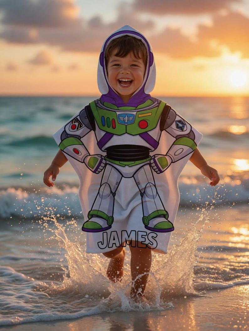 May include: A white hooded beach towel with a Buzz Lightyear costume design, featuring green, purple, and white details. The towel displays a graphic of the character's spacesuit and the name "JAMES". The child is in the water, with the sea and sunset in the background.