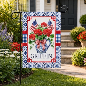 May include: A decorative garden flag featuring a floral arrangement in a blue and white vase, two American flags, and the name "GRIFFIN". The flag has a red, white, and blue color scheme with a gingham pattern and floral border.