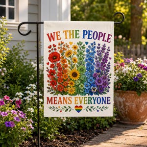 May include: A garden flag with the text "WE THE PEOPLE MEANS EVERYONE" in rainbow colors. The flag features a floral design with flowers in a rainbow of colors, including red, orange, yellow, green, blue, and purple. A rainbow heart is at the bottom.