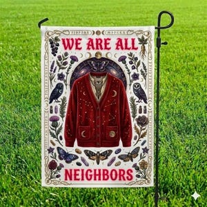 May include: A garden flag with the text "WE ARE ALL NEIGHBORS" in red. The flag features a red cardigan with celestial and occult imagery, including butterflies, owls, and constellations. The flag is displayed on a black metal garden stake.