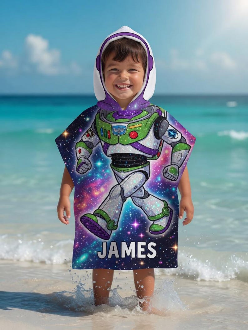 May include: A hooded beach towel featuring a colorful graphic of Buzz Lightyear from Toy Story, with a space-themed background. The towel has a white hood with purple trim and the name "JAMES" printed on the bottom.