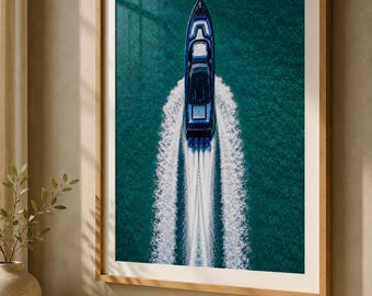 Puede incluir: Una impresión de arte mural vertical enmarcada que muestra una vista aérea de una lancha motora azul oscuro navegando sobre aguas turquesas profundas, creando una estela blanca marcada. La impresión tiene un marco de madera clara y paspartú blanco.