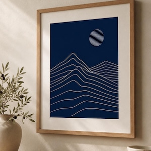 May include: A framed wall art print featuring a deep navy blue background with white line art depicting a mountain range and a circular sun composed of horizontal lines. The artwork is enclosed in a light-toned wooden frame with a white mat border.