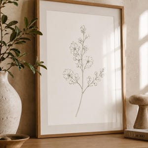 May include: A framed wall art print featuring a delicate black line drawing of a flowering botanical branch with multiple blossoms and buds on a white background, encased in a light-toned wooden frame with a white mat border.