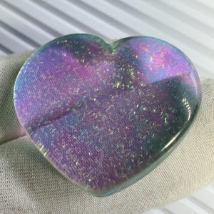 May include: A heart-shaped ornament with an iridescent finish. The colours shift from purple to blue and green, with sparkling highlights. The object is smooth and appears to be made of glass or a similar material.