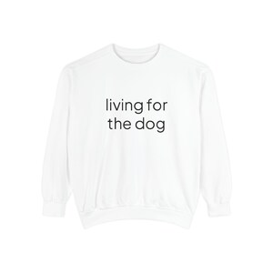 May include: A white long-sleeve sweatshirt featuring the black text "living for the dog" printed in a simple sans-serif font across the center of the chest. The garment has a crew neckline, ribbed cuffs, and a ribbed hemline at the bottom.