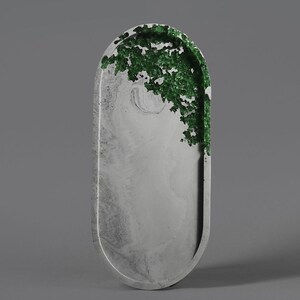 Op de afbeelding: Een ovaalvormige decoratieve schaal met een gemarmerd grijs oppervlak en een getextureerd groen accent aan één uiteinde. De schaal heeft een gladde, afgeronde rand en een minimalistisch ontwerp, geschikt voor interieurdecoratie.