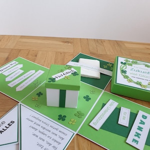 Könnte beinhalten: Eine grüne und weiße Geschenkbox mit Kleeblatt-Design, umgeben von grünen Karten mit Text und Kleeblatt-Akzenten. Die Karten entfalten sich und zeigen mehr Text und eine kleine Geschenkbox. Das Gesamtthema ist ein festliches Geschenk.