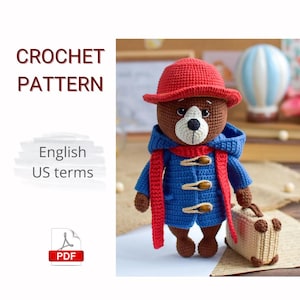 May include: A crocheted bear wearing a red hat, blue coat, and red scarf, holding a small suitcase. The bear has a brown body, a white muzzle, and is made with US crochet terms. The image includes the text "CROCHET PATTERN" and "English US terms".
