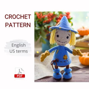 Op de afbeelding: Gehaakte vogelverschrikkerpop in blauw en geel met een puntmuts en gestikte gezichtskenmerken. De pop heeft garen haar en beige handschoenen en laarzen. De tekst "CROCHET PATTERN" en "English US terms" is inbegrepen.