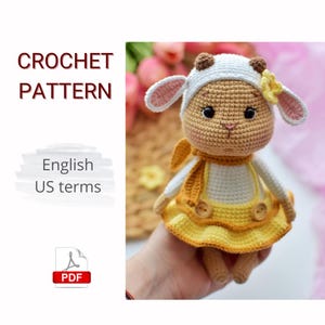 May include: A crocheted sheep doll wearing a yellow dress with a white top and a matching scarf. The doll has a white hat with brown accents and pink-lined ears. The image includes the text "CROCHET PATTERN" and "English US terms".