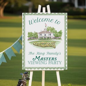 May include: A white easel displays a sign that reads "Welcome to The King Family's Masters Viewing Party." The sign features a watercolor illustration of a building and a golf course. A golf bag, golf balls, and floral arrangements are on the green grass.