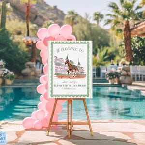 May include: A wooden easel displays a sign with the text "Welcome to The King's 152nd Kentucky Derby Celebration." The sign features a horse race illustration, surrounded by a green border. Pink balloons decorate the scene near a pool.