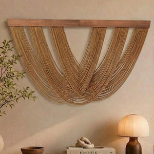May include: A wall hanging featuring a horizontal wooden bar with numerous tan cord strands draped in multiple U-shaped layers. The cords create a symmetrical, cascading pattern across the wall, suspended from the straight wooden support beam.