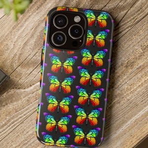 May include: A black smartphone case featuring a repeating pattern of colorful butterflies. The butterflies have rainbow-colored wings and are set against a black background. The case is on a wooden surface.