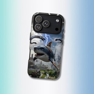 May include: A black smartphone case featuring a graphic print of a large shark flying over a city landscape with lightning bolts and dark, swirling clouds in the background. The case has a cutout for the camera lenses and flash on the top back.