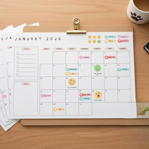 May include: A 2026 January calendar with colorful stickers and emoji-style icons, held by a gold clip. Additional calendar pages are stacked to the left. A mug with a paw print, a notebook, and glasses are on the right.