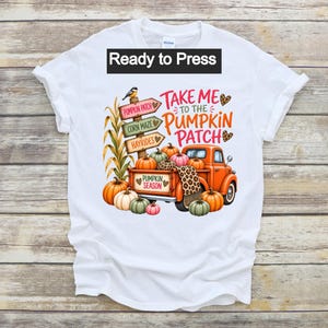 May include: A white t-shirt featuring a graphic print of an orange truck filled with pumpkins, a wooden signpost with the text 'PUMPKIN PATCH', 'CORN MAZE', and 'HAYRIDES', and the text 'TAKE ME TO THE PUMPKIN PATCH' and 'PUMPKIN SEASON'.