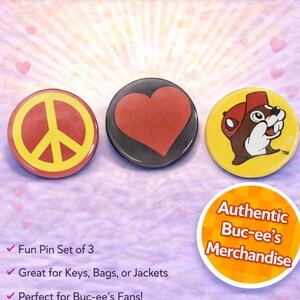 May include: A set of three Buc-ee's collector button pins. The pins feature a peace sign, a red heart, and the Buc-ee's beaver mascot. The pins are yellow, red, black, and white. The text "Authentic Buc-ee's Merchandise" is also visible.