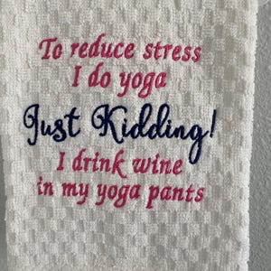 May include: White, textured towel with embroidered text in pink and navy blue. The text reads "To reduce stress I do yoga Just Kidding! I drink wine in my yoga pants."