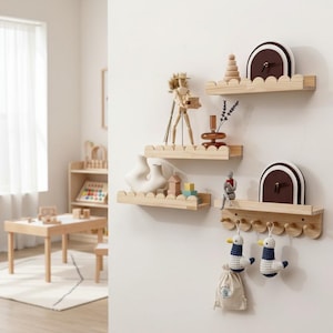 Puede incluir: Tres estantes de madera con bordes festoneados montados en una pared blanca. Los estantes exhiben objetos decorativos como un reloj de madera, un maniquí de artista de madera y un jarrón blanco. Debajo, un perchero de madera sostiene dos adornos de pato y una bolsa pequeña.