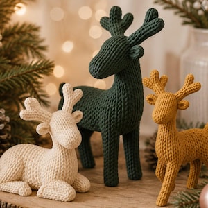 Könnte beinhalten: Drei gestrickte Hirschfiguren in Creme, Dunkelgrün und Senfgelb. Der cremefarbene Hirsch liegt, während der dunkelgrüne und der senfgelbe Hirsch stehen. Jede Figur weist ein strukturiertes Strickmuster und ein Geweih auf.