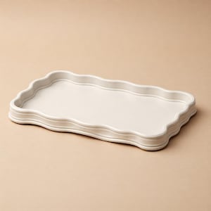 May include: An off-white rectangular serving tray with a scalloped edge. The tray has a raised base with decorative trim. The interior surface is smooth and flat. The tray is designed for serving food or displaying items.