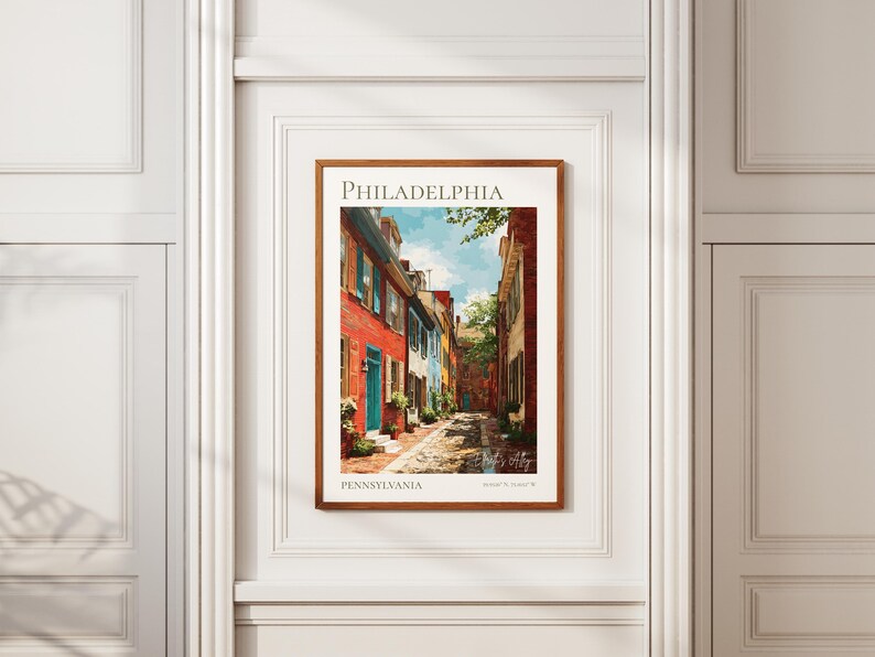 May include: A framed art print of a Philadelphia street scene. The print features colorful row houses in red, blue, and white, with a cobblestone street. The word "PHILADELPHIA" is at the top, and "PENNSYLVANIA" is at the bottom.