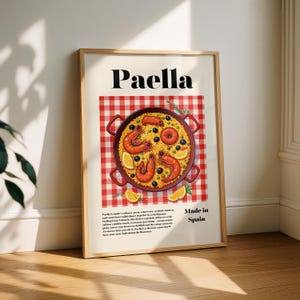 Puede incluir: Un póster enmarcado con una ilustración de paella, un plato de arroz español. La imagen muestra una sartén roja llena de arroz, gambas, salchichas y verduras, sobre un fondo a cuadros rojos y blancos. La palabra "Paella" está en la parte superior.