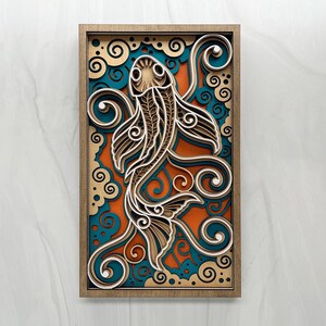 May include: A rectangular layered wood wall art piece featuring a stylized koi fish design. The artwork consists of stacked laser-cut panels in shades of natural wood, vibrant orange, and deep teal, creating a three-dimensional depth effect.
