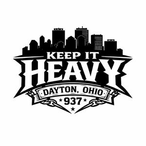 May include: Black and white graphic featuring a city skyline silhouette above the words "KEEP IT HEAVY" in bold letters. Below, it reads "DAYTON, OHIO" with "937" and star accents. The design has a strong, edgy aesthetic.