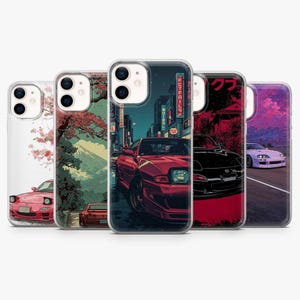 May include: Five phone cases with Japanese car-themed artwork. Designs include a red car in a night city scene, a black car, and a white car with cherry blossoms. Each case has a clear border, offering protection while displaying the artwork.