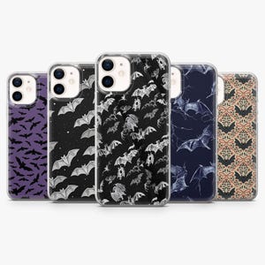 May include: Five phone cases with bat designs. The cases display bat patterns on backgrounds of purple, black with stars, black and white, navy blue, and a floral design. The cases are for a mobile phone.