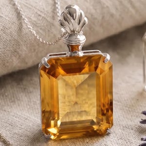 May include: A silver pendant necklace featuring a large, rectangular, faceted citrine gemstone. The gemstone is a warm, golden-yellow color and is set in a silver frame. The pendant hangs from a delicate silver chain.